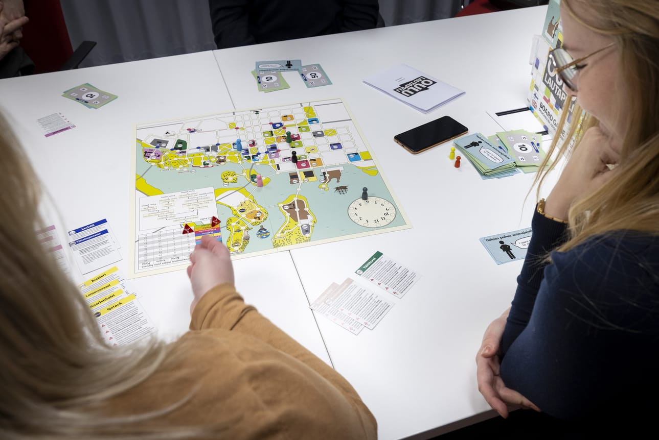 Anna Poropudas (vas.) ja Krista Huttu tarkastelevat Oulun keskustan ruutukaava-alueesta koostuvaa pelilautaa.