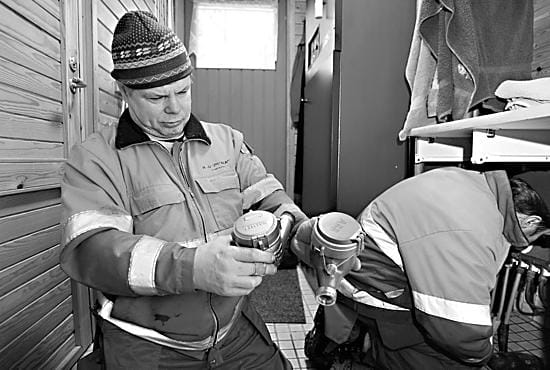 Uusi sinikantinen. Haukiputaan vesihuollon asentaja Einari Suutari katsastaa vanhan (vas.) ja uuden vesimittarin eroja. Asentaja Mika Päkkilä valmistelee jakotukkia asennukseen.