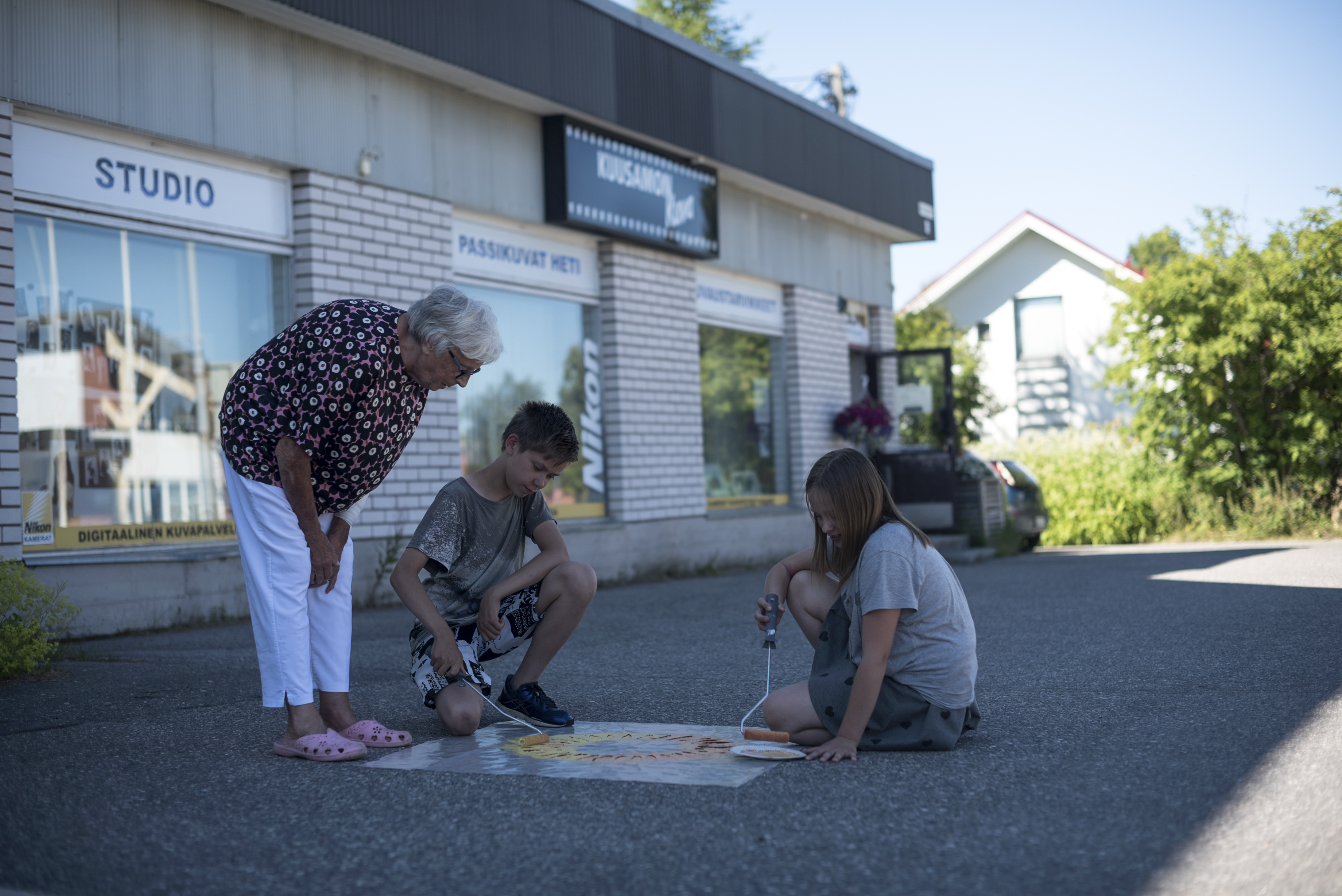 Liisa Kinnunen katsoo, kun lapsenlapset Arttu Kinnunen ja Alisa Kinnunen taiteilevat pihalle auringonkukat.