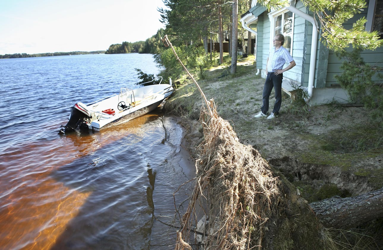 Hiekkaranta hävisi, puut kaatuivat ja vene särkyi, kun liian korkealla lainehtiva vesi sai lisävoimaa myrskystä. Heikki Leppäniemi odottaa kivikuormaa rantansa suojaksi.