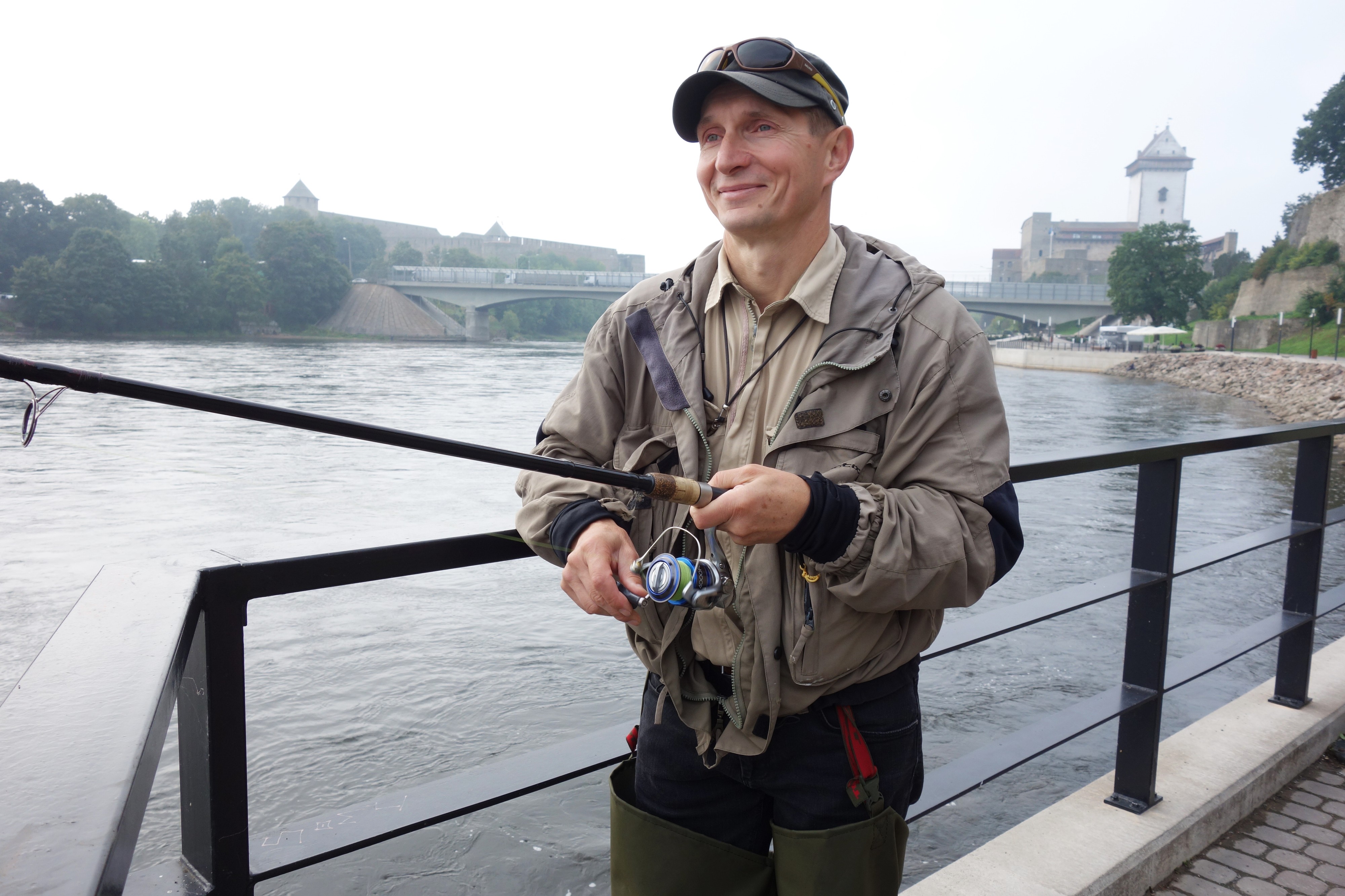 Narva-joki houkuttelee kalastajia. Sergei Muhhin heittää viehettä rantapromenadin ulokkeella. Osa kalastajista on ankkuroinut veneensä virtaan. Joessa kelluu punaisia poijuja merkkeinä Venäjän rajasta. Rajan ylityksestä tulee 800 euron sakko. Takana vasemmalla Venäjän Iivananlinna, oikealla Viron Narvan linna.