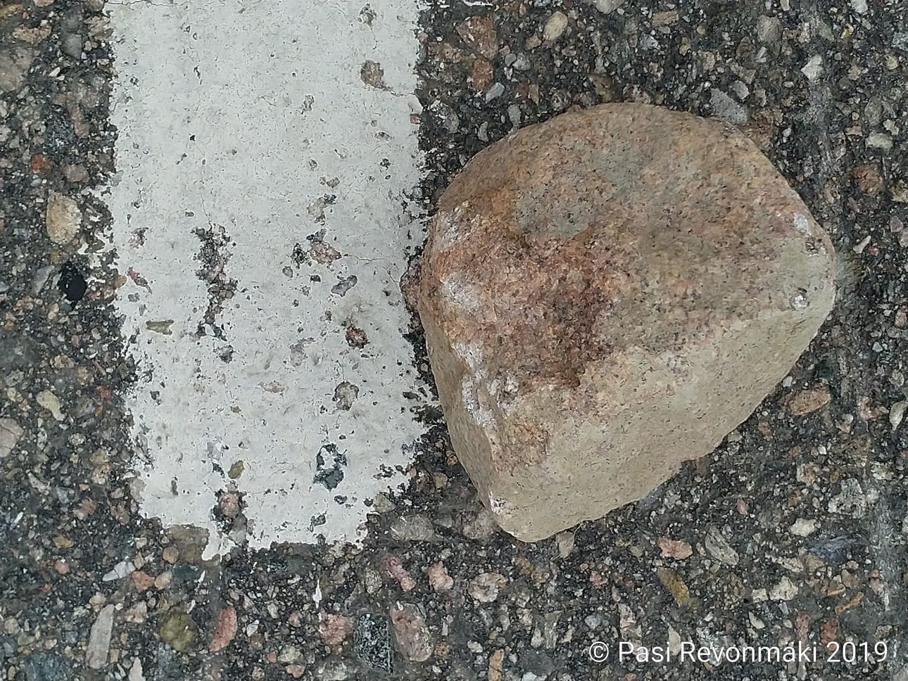 Pasi Revonmäen tiellä löytämässä kivessä vasemmassa reunassa näkyy iskeymäjälkiä. Kaistan reunaviiva antaa kivelle mittakaavan.