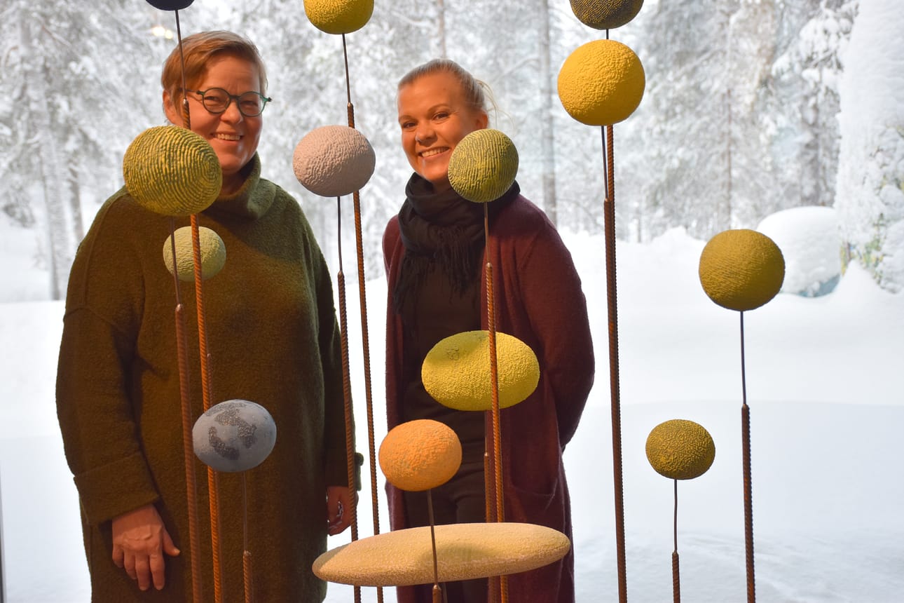 Kuusamon ja Posion myymäläpäällikkö Mervi Tornberg-Karjalainen (oik.) kiviaiheisia esineitä valmistaneen Riitta Talonpojan kanssa meteoriittisateen keskellä.