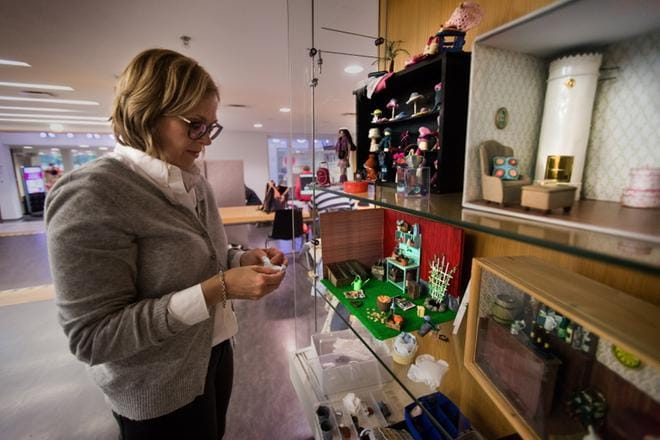 Satu Kiviniemi asettelemassa näyttelyä kaupunginkirjastossa. Vitriineissä voi ihailla muun muassa hattukauppa Unelma-asustetta sekä kamiinalla varustettua tunnelmallista makuuhuonetta. KUVAT: JARNO PELLINEN