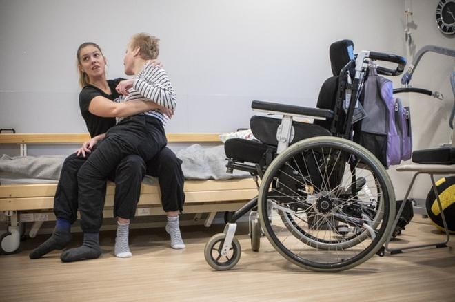 Fysioterapeutti Anne Kurhela avustaa Jouni Alataloa, 17, siirtymään vuoteesta pyörätuoliin. Nosturin käytön sijaan annetaan Alatalon tehdä mahdollisimman paljon itse. KUVAT: MARJUT KRIIKKU