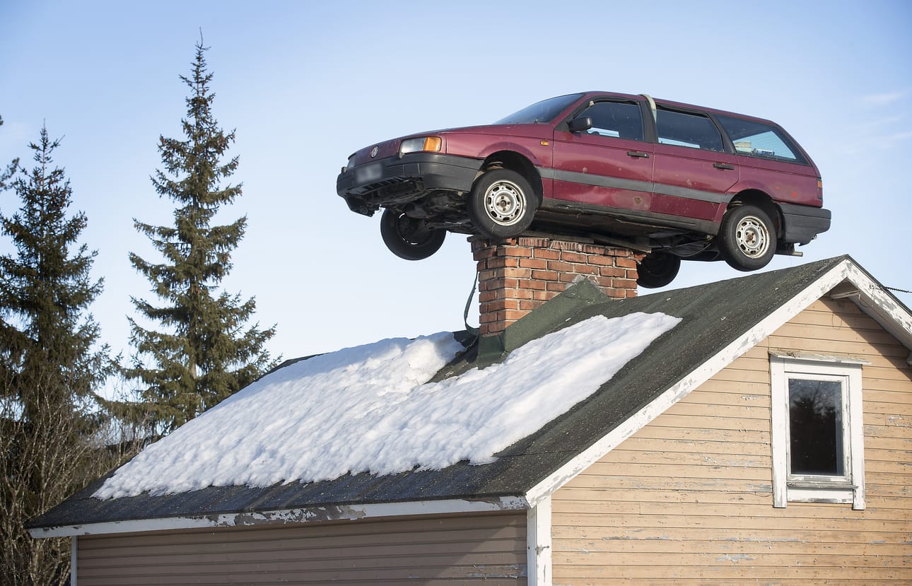Yli-Iissä maalaistalon katolle piipun päälle on nostettu farmariauto.