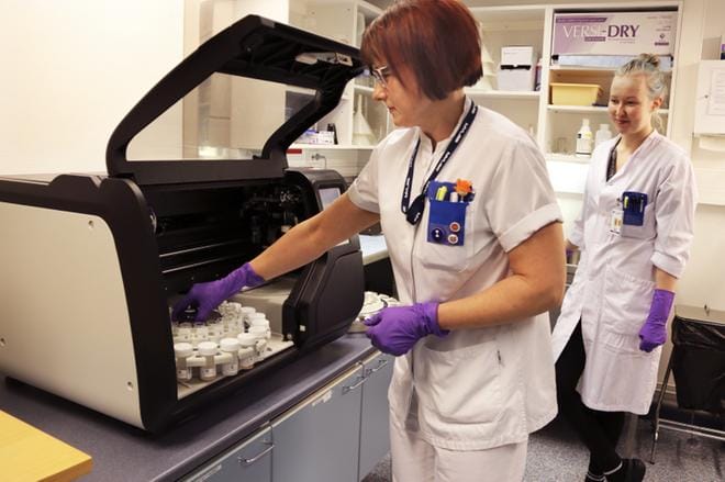 Laboratorionhoitaja Johanna Paalanen ja solubiologi Monica Nieminen pyörittävät näytepurkkien karusellia päivittäin. Kerrallaan laite voi käsitellä 20 näytettä tunnissa. Kuva Outi Rantala