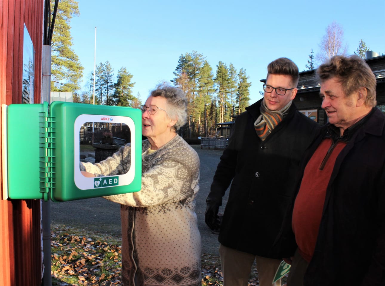 Ulla ja Olavi Viitakoski sekä Juha Herrala Sarviluoman entisen kyläkoulun vieressä Isojoella. Yksi uusista sydäniskureista tulee rakennuksen ulkoseinään. Kuva.