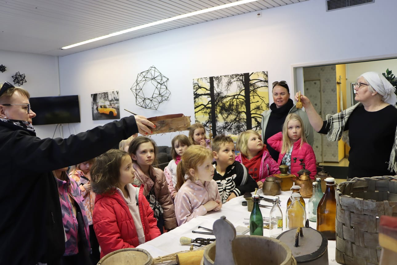 Marttojen Sirpa Joutsenlahti (oik.) esittelee pientä tuohesta tehtyä esinettä, jossa on säilytetty suolaa. 1A-luoka opettaja Riitta Lehtinen näyttää vasemmalla tuohirovetta, jonka ulkonäköä matkitaan nykyään pahvisiin mämmiastioihin.