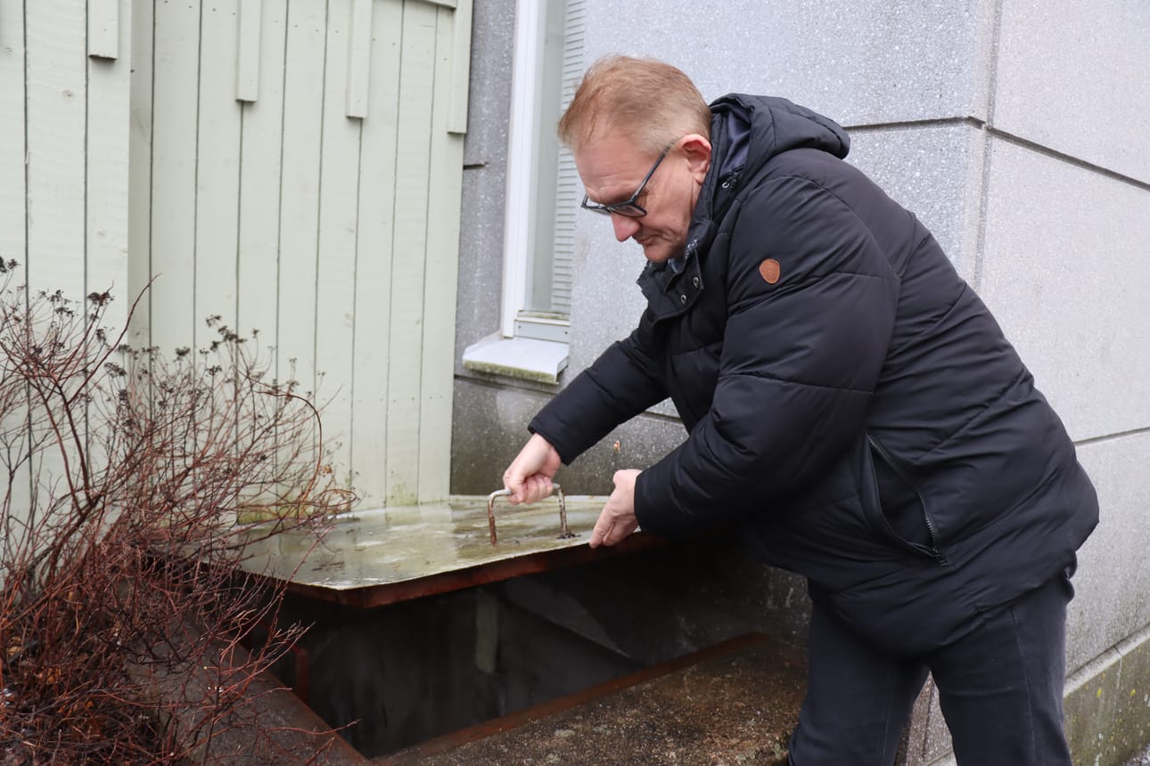 Isännöitsijä Leif Norrgård näyttää, miten väestönsuojan varauloskäytävää suojaava luukku avautuu nostamalla ulkopuolelta.