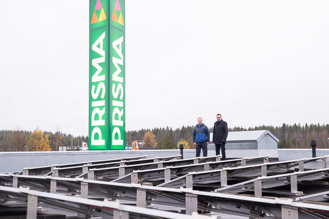 Koillismaan Osuuskaupan talousjohtaja Esa Niinisalo (vas.) ja toimitusjohtaja Harri Lämsä Kuusamon Prisman aurinkovoimalalla. Harjakattoinen rakennelma miesten takana on savunpoistoluukku.