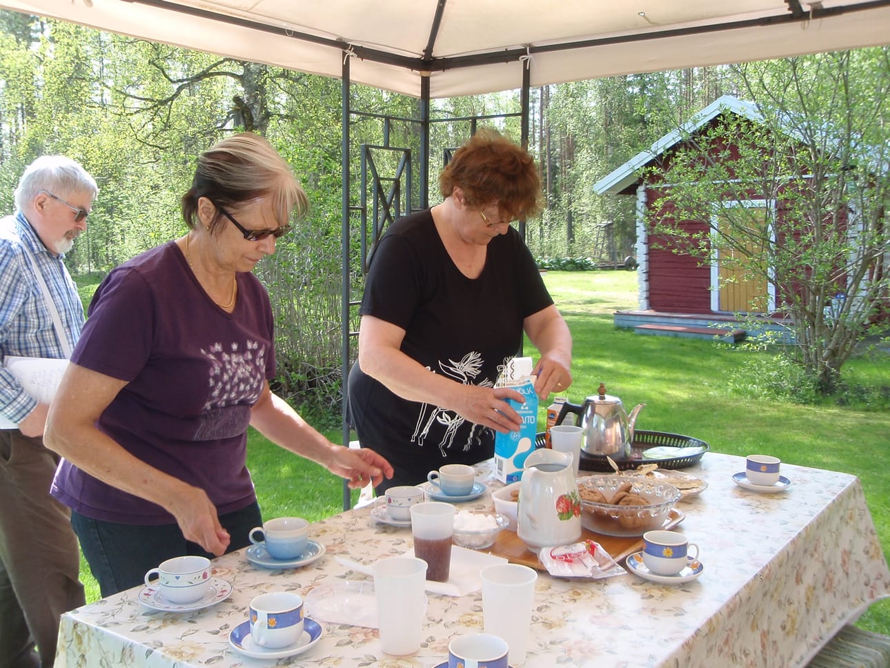 Ojalan kaksosten vaimot Maija (vas.) ja Eira kattavat pihamaalla runsasta kahvipöytää yllätysvierailleen.